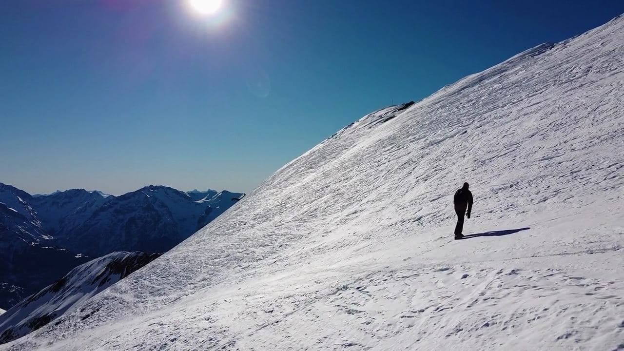 Climber walking up a snow-covered mountain ridge toward distant peaks